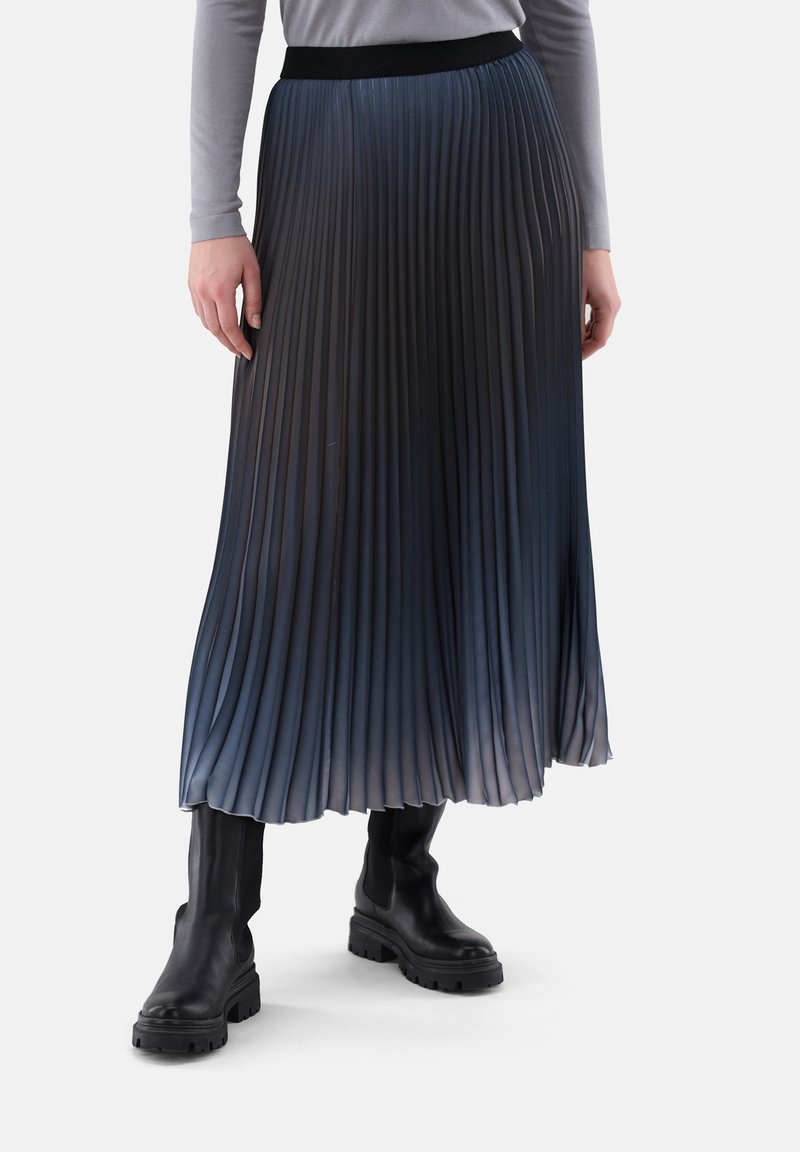 Pleated midi skirt in a gradient blue, featuring a black elastic waistband. Textured fabric with vertical folds, paired with black ankle boots.
