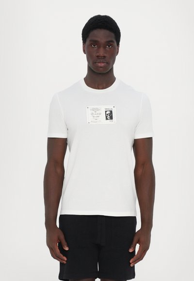 White cotton t-shirt featuring a black and white graphic print in the center. Short sleeves and a round neckline.