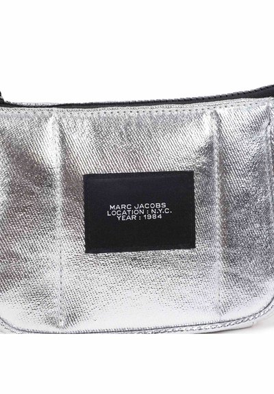 Ασημένια μεταλλική τσάντα με υφή στην επιφάνεια, μαύρη ετικέτα με λευκό κείμενο: "MARC JACOBS LOCATION: N.Y.C. YEAR: 1984."