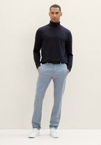 Navy turtleneck sweater, light blue trousers, and white sneakers. The sweater has a fitted design; trousers are relaxed with pockets.