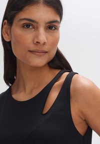 Zwarte mouwloze top met een ronde halslijn en uitsnijdingen bij de schouders. Glad, rekbaar materiaal met een aansluitend ontwerp.