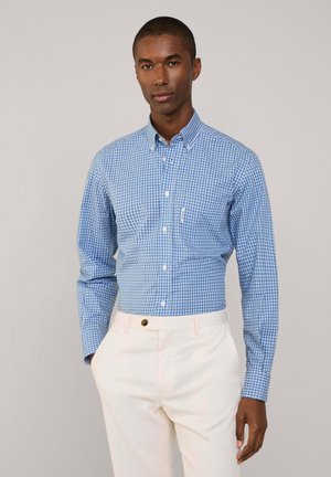 Camicia button-up a quadri blu e bianchi con colletto, maniche lunghe e taschino sul petto, indossata con pantaloni color crema.