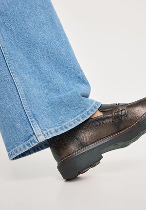 Bruine leren schoen met een lage hak, gecombineerd met brede lichtblauwe denim jeans met een rafelige zoom.