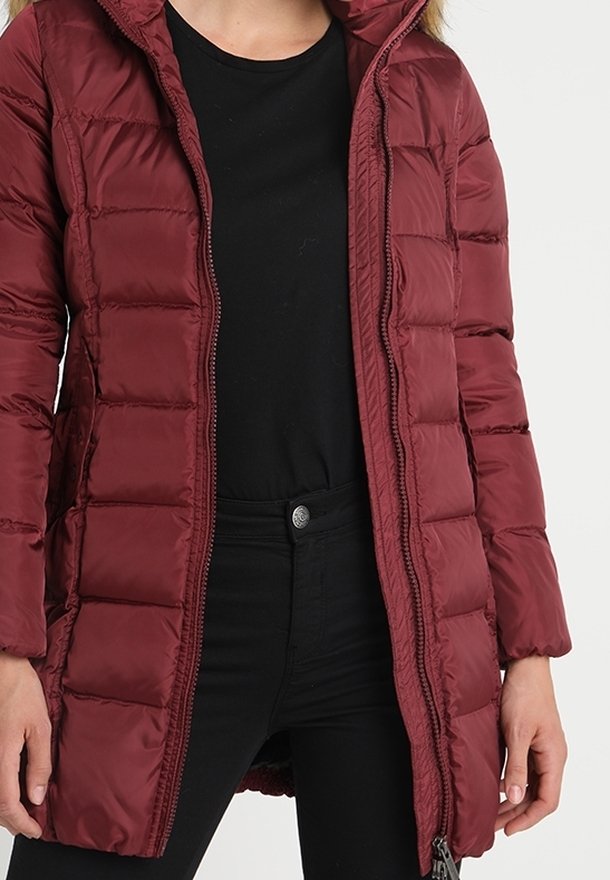 Chaqueta acolchada burdeos con cierre de cremallera frontal, capucha y diseño acolchado. Tejido suave con detalles de costuras; combinada con una camiseta negra.