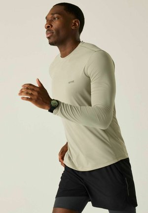 Hombre corriendo en interior vistiendo camiseta de manga larga beige claro, pantalones cortos negros y reloj inteligente negro en la muñeca izquierda.