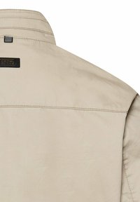 Beige Baumwolljacke Rückseite mit gestepptem Kragen, horizontaler Naht und kleinem schwarzem "Camel Active" Markenlabel nahe dem Kragen.
