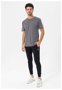Grå kortærmet t-shirt med rund halsudskæring, parret med sorte tapered joggers med et lille logo. Hvide træningssko fuldender looket.