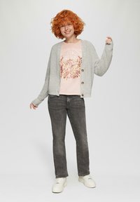 Szary wełniany kardigan zapinany na drewniane guziki, noszony na różowej koszulce z kwiatowym motywem, w zestawieniu z szarymi dżinsami i białymi sneakersami.