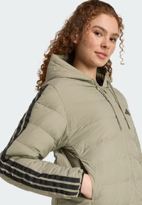 Bundička s kapucňou v svetlej olivovej farbe, so zipsom a čiernymi pruhmi na rukávoch. Hladký povrch s prešívaným vzorom.