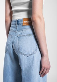 Lichtblauwe denim jeans met een losse pasvorm, voorzien van een oranje leren label op de tailleband en twee achterzakken met contrasterende stiksels.