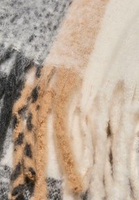 Uldnaturstrik med en kombination af grå, beige og cremefarver, med bløde, teksturerede fibre og frynser i kanten.