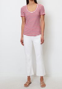 Rød- og hvidstribet t-shirt med korte ærmer og v-hals, parret med hvide flarebukser og flade sandaler. Enkel, afslappet outfit.