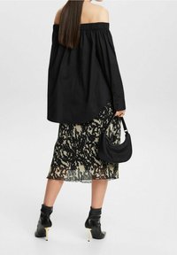 Blusa negra sin hombros, falda plisada con un patrón abstracto en negro y crema, botines con tacones dorados y un pequeño bolso negro.