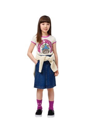 White t-shirt with pink trim featuring graphic print, paired with a blue denim skirt, cream sweater tied at the waist, and purple socks.