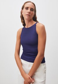 Top da donna a canotta ribbed blu navy con un design aderente, caratterizzato da spalline larghe e scollatura rotonda, abbinato a pantaloni chiari.