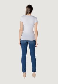 Witte, aansluitende T-shirt met korte mouwen gecombineerd met blauwe skinny jeans. Het T-shirt is glad, terwijl de jeans zakken hebben en een lichte stretch bieden.