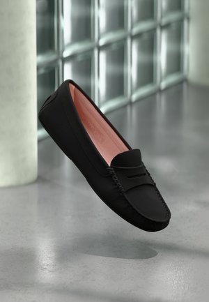 Czarne skórzane loafersy o miękkiej teksturze, różowe wykończenie wewnętrzne, dekoracyjne przeszycia i zaokrąglony czubek. Unoszą się na neutralnym tle.