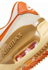 Sneaker arancione e crema con tomaia in pelle testurizzata, ammortizzazione Air Max visibile e suola in gomma con battistrada a motivo.