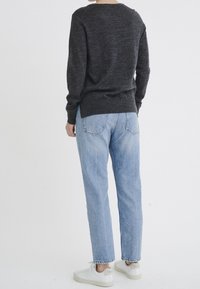 Pull à manches longues gris foncé, coupe ample, accompagné de jeans taille haute bleu clair et de baskets blanches. Design minimaliste, sans motifs.