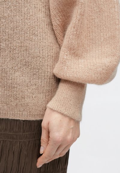 Világos rózsaszín kötött pulóver struktúrált felülettel, ballon ujjakkal és testhezálló mandzsettákkal, barna pliszírozott szoknyával párosítva.