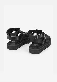 Sandalias de plataforma de cuero negro con múltiples correas y una cremallera trasera, que presentan un acabado texturizado y una suela de goma gruesa.