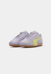 Purple suede sneakers with yellow accents and logo, featuring a gum rubber sole and classic lace-up design. Curved side panels enhance shape.