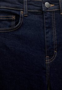 Jean en denim bleu foncé avec des coutures dorées contrastantes, une poche avant et un bouton métallique visible à la taille.