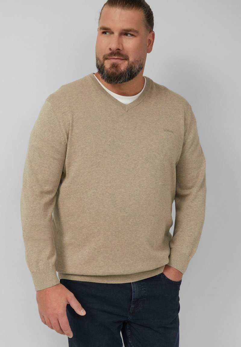 Beige V-hals truien gemaakt van zachte stof, met lange mouwen en ribgebreide manchetten, gedragen over een wit shirt. Donkere jeans maken de outfit compleet.
