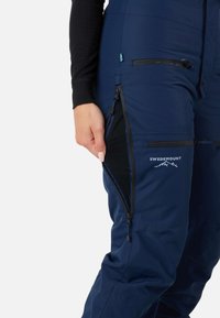 Marineblauwe Swedemount-broek met een ritszak aan de zijkant en meshvoering, met een slanke, gladde textuur en logo op de dij.