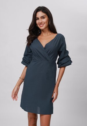 Robe bleu foncé avec un décolleté en V profond, des manches trois-quarts avec des détails en volants et une silhouette ajustée. Texture lisse.