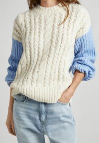 Kermanvärinen ja vaaleansininen palmikkoneulepusero, jossa resorit hihoissa ja helmassa. Koristelee teksturoitu kuvio ja laskostetut olkapäät; pehmeä, paksu muotoilu.