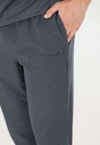 Graue Sporthosen aus leichtem Material. Mit einer Seitentasche und dem schwarzen "ENDURANCE"-Logo in der Nähe des Taillenbunds. Glatte Textur.