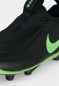 Μαύρο και πράσινο παπούτσι ποδοσφαίρου Nike με υφασμένο επάνω μέρος, πράσινο λογότυπο Nike και διαμορφωμένες αγκράφες στη σόλα για παιχνίδι σε τεχνητό χλοοτάπητα.