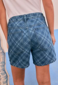 Denim shorts met een blauw geruit patroon, voorzien van achterzakken en een tailleband. De stof heeft een gestructureerde uitstraling met vervaagde accenten.