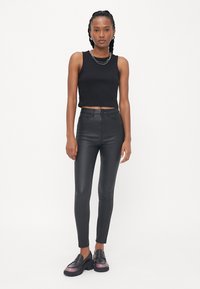 Zwarte fitted crop top gecombineerd met hoge zwarte leren achtige broek. Model draagt chunky zwarte schoenen met een roze accent.