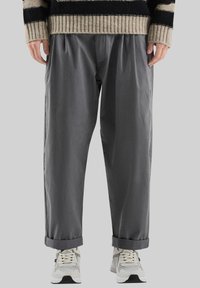 Pantalons gris, coupe décontractée avec une taille et des plis, présentant des revers et une texture lisse, associés à des baskets blanches.