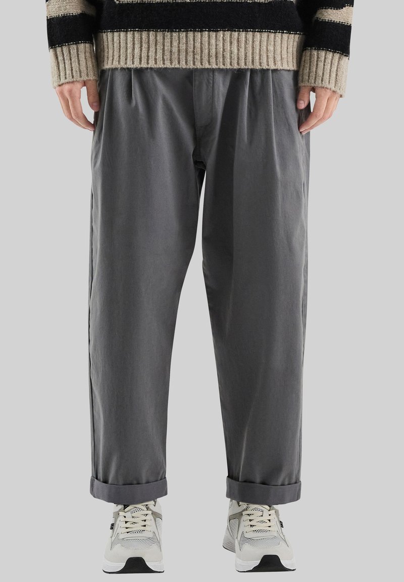 Grijze, relaxte broek met een tailleband en plooien, voorzien van opgerolde pijpen en een gladde textuur, gecombineerd met witte sneakers.