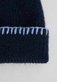 Navy knitted beanie with ribbed texture and light blue contrast stitching along the edge, featuring a snug, rounded design.