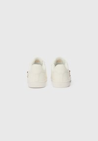 Baskets blanches en cuir avec un intérieur doux, semelle en caoutchouc plate et design minimaliste. Présente un petit logo discret près du talon.