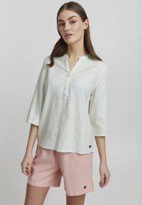 Lys grøn, skjort i linned med krave og trekvartærmer samt knapper foran, parret med lyserøde linnedshorts med sidelommer og detaljer.