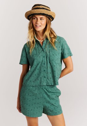 Groene katoenen set bestaande uit een blouse met korte mouwen, knopen en een zak, en bijpassende shorts, beide met opengewerkte patronen en een losse pasvorm.