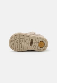 Semelle de chaussure beige clair avec des motifs en caoutchouc texturé. Présente un logo marron et un accent circulaire. Conçue pour l'adhérence et le confort.