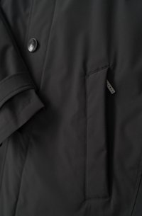 Schwarze Puffjacke aus glattem Material mit Knopfverschluss und einer Seitentasche mit einem kleinen Etikett. Das Design umfasst einen strukturierten Kragen und Ärmel.