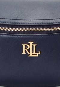 Saco de couro azul-marinho com fecho em zíper dourado e destacado logótipo "RL" em dourado. Textura suave com costuras visíveis. Design compacto.