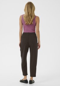 Brown tailored pants with a relaxed fit, side pockets, and rear detailing. Paired with a light purple tank top and black shoes.