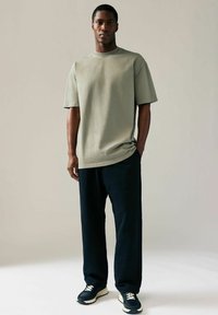Olivgrön t-shirt med kort ärm, avslappnad passform, ihop med marinblå vida byxor och mörka sneakers med ljus sula.