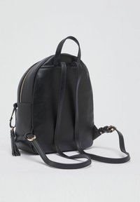 Sac à dos en cuir noir de forme arrondie, avec une fermeture éclair dorée, une poche latérale et des bretelles réglables. Dispose d'un détail à pampille sur le côté.