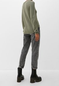 Pull vert en maille côtelée à manches longues, associé à un jean gris texturé et des bottines noires à talons. Tous les articles sont ajustés.