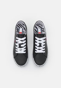 Pár černých kožených tenisek s bílými tkaničkami a podrážkami, se středními vložkami s proužky zebry a červenými, bílými a modrými značkovými štítky na stranách.