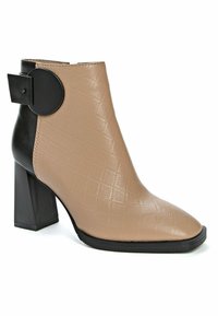 Bota de tobillo de cuero sintético beige con textura acolchada, punta puntiaguda y tacón grueso negro. Cuenta con un detalle redondo negro cerca del tacón.